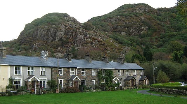 a terrace of small welsh cottages on a neat village green below sharp angular rocky hills